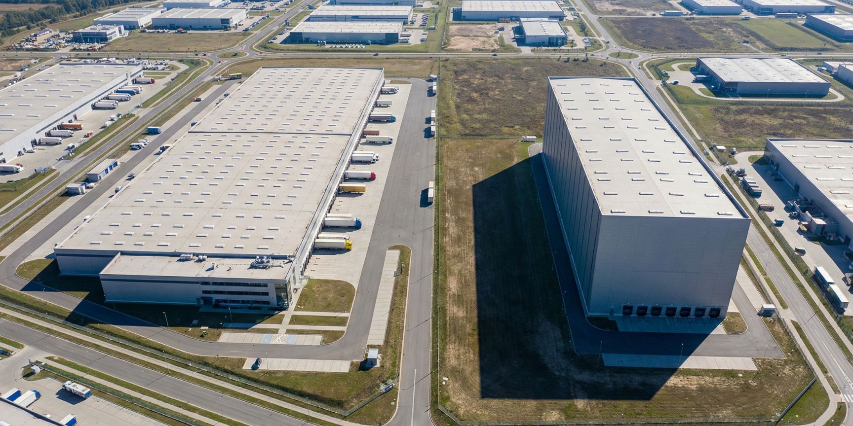 Luftaufnahme eines Industriegebiets zeigt den Vergleich zwischen einem flachen, weitläufigen Logistiklager (links) und einem hohen, kompakten Hochregallager (rechts), was unterschiedliche Baumassenzahlen (BMZ) illustriert